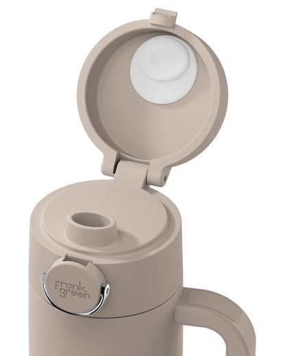 A close-up of a beige insulated bottle with its lid open, showing a white inner lid and a silver metal ring around the flip-top opening. The brand name 'frank green' is printed on the silver ring.