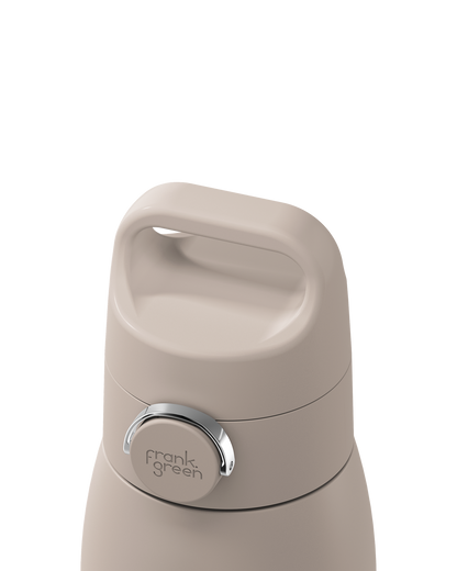 Close-up of a beige insulated bottle lid with a carry handle and a silver circular button featuring the frank green logo, set against a solid white background.