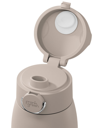 A close-up of a beige insulated bottle with its flip-top lid open, showing the white inner lid and a small silver metal loop. The brand name 'frank green' is printed on the silver loop.