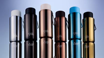 Six metallic travel tumblers with different colors (silver, black, rose gold, bronze, blue, and gold) lined up vertically on a reflective surface against a blue gradient background. The brand name 'frank graham' is printed near the bottom of each tumbler.
